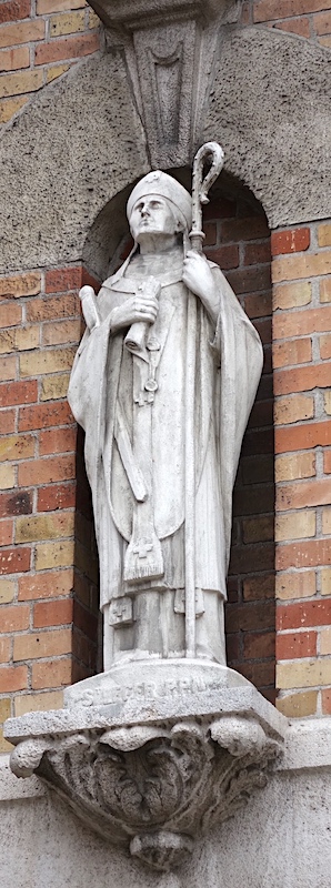 On distingue à gauche une abbaye et, en haut, les instruments de son supplice puisqu'il eut les lèvres et la langue coupées - Eglise Saint Léger - Lens 62